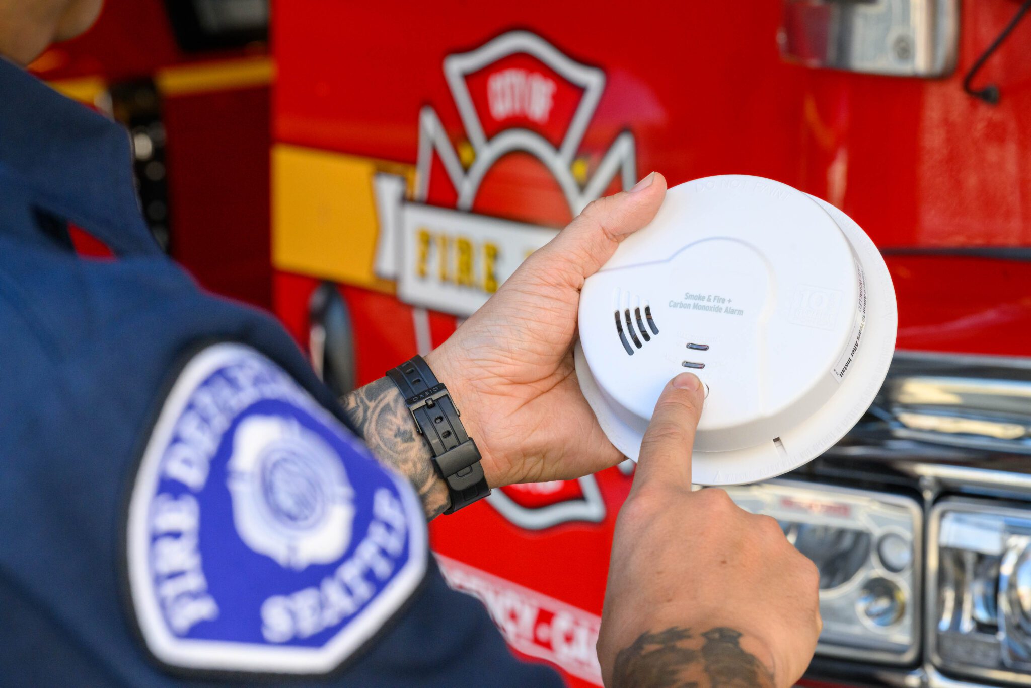 Firefighter holding a white smoke alarm in front of a red fire engine