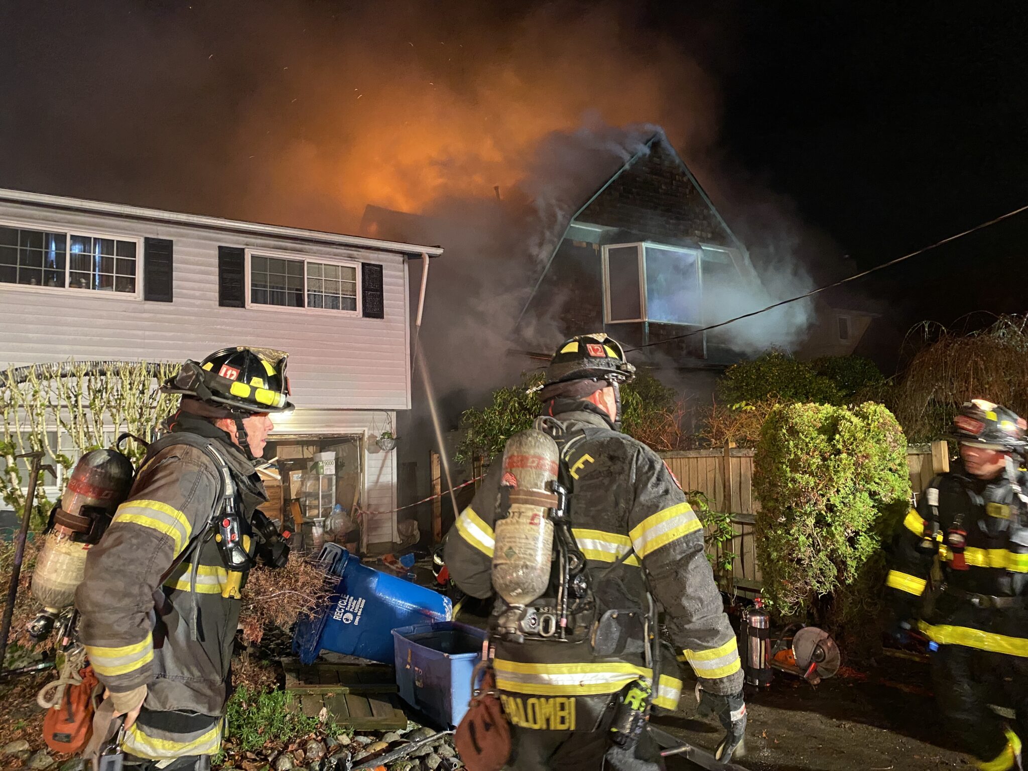 Firefighters protecting a neighboring home from a fire.