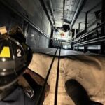 Firefighter looks down elevator shaft as crews work below to rescue occupants from elevator car.