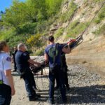 Firefighters hold Stokes basket containing patient being lowered from hillside.