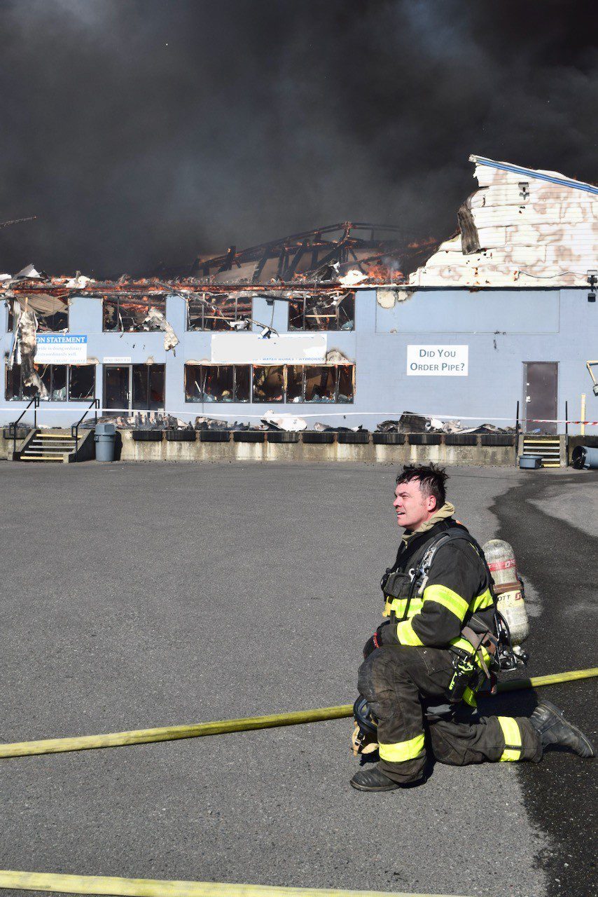 Firefighter kneels in front of the fire building.