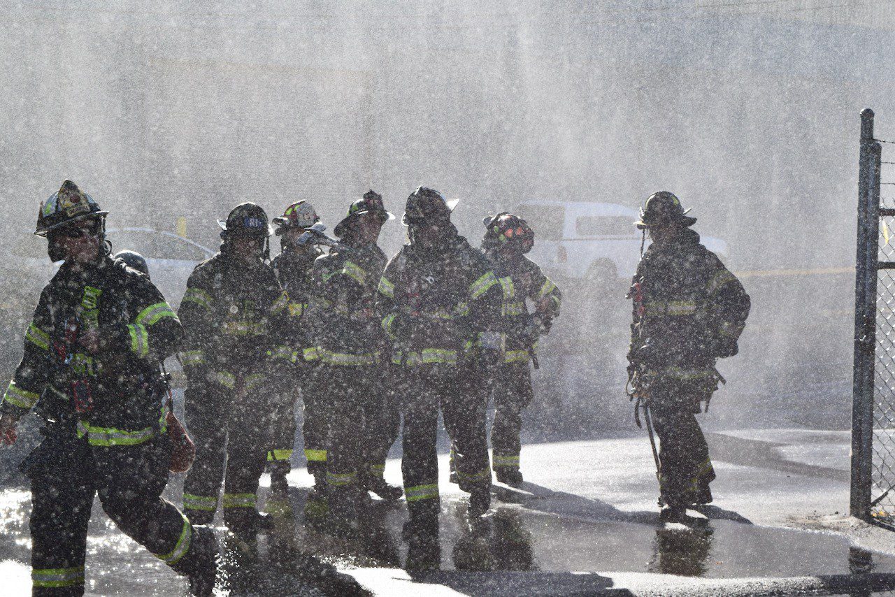 A group of firefighters stand in a spray of water.