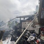 Firefighters spray water on smoldering debris in backyard.