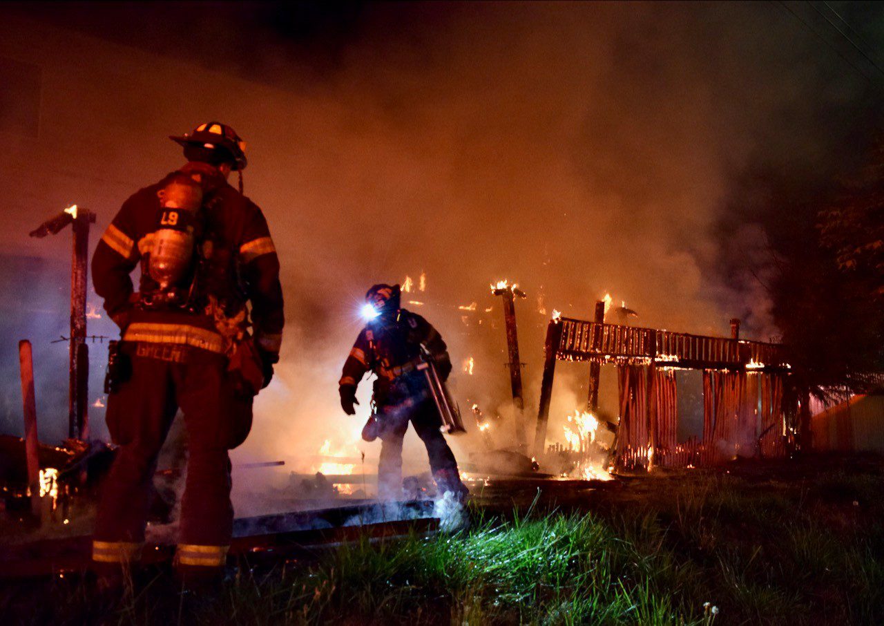 Firefighters run toward fire, flames visible.