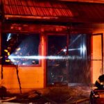 Firefighters shine flashlights into burned structure.