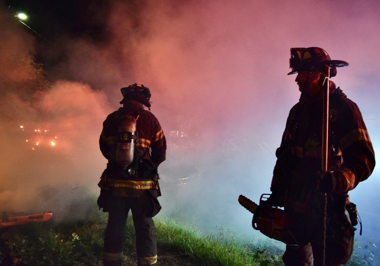 Firefighter holds chainsaw standing next to another firefigther.